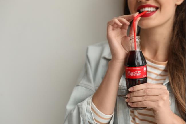 אישה צעירה שותה קוקה קולה, דבר שעלול להעלות את הסיכון ללקות בסרטן המעי 
